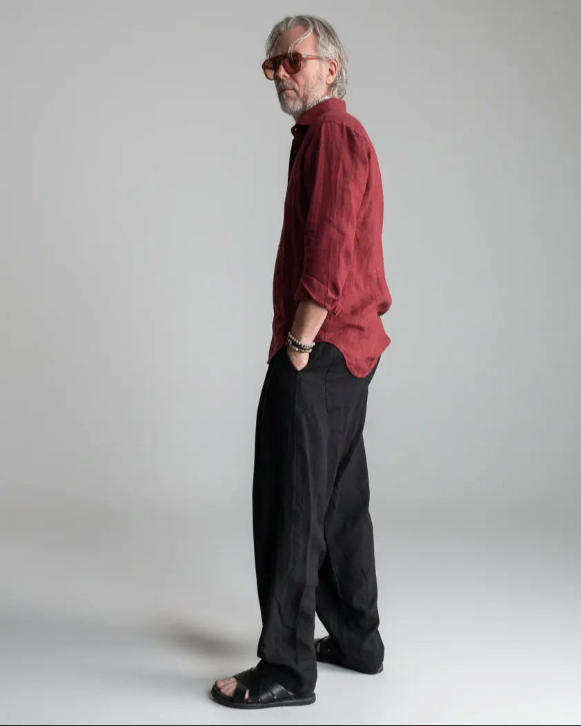 Man in a black pants and red linen shirt  standing against light grey backdrop