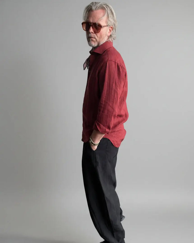 Man in a black pants and red linen shirt  standing against light grey backdrop