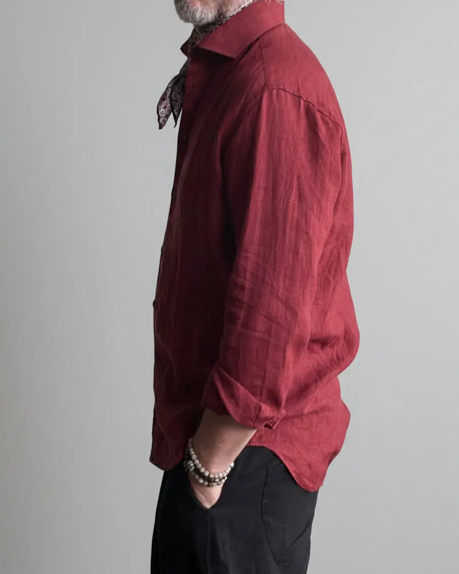 Man in a black pants and red linen shirt  standing against light grey backdrop