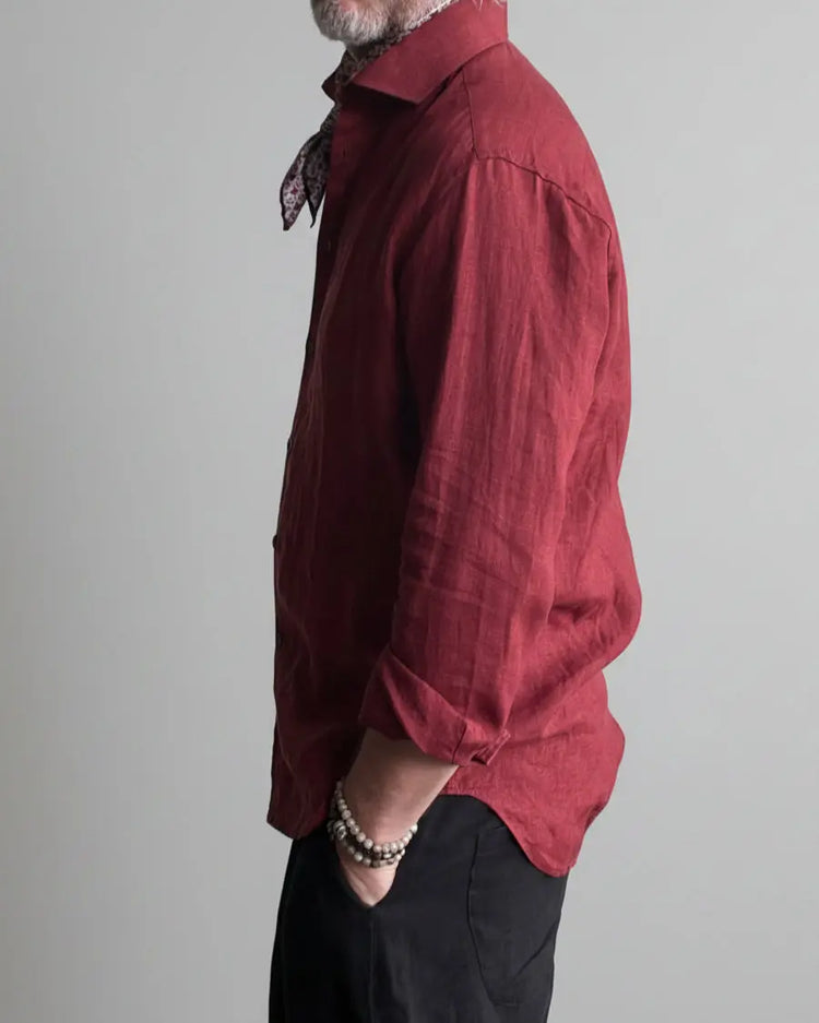 Man in a black pants and red linen shirt  standing against light grey backdrop