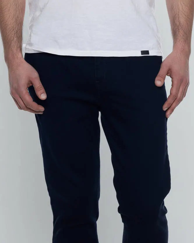 Model wearing navy blue chinos and a white shirt on a grey backdrop