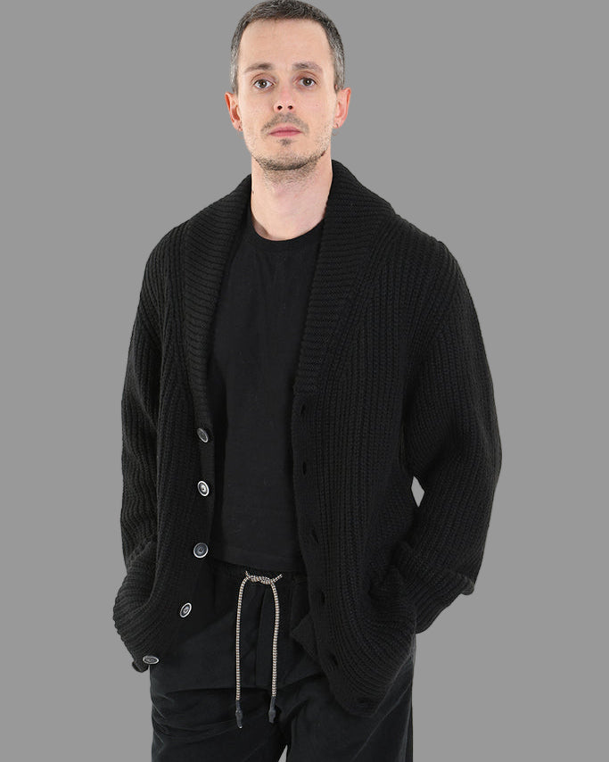 Man wearing a black ribbed cardigan over a black shirt with a white background